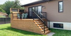 a house with a deck and stairs leading up to the front door, next to a fenced in yard