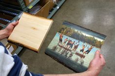 a person holding a wooden box with a painting on it in the middle of a room