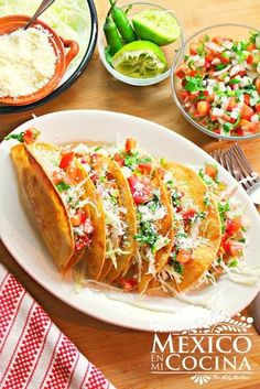 several tacos on a white plate next to bowls of salsa and tortillas