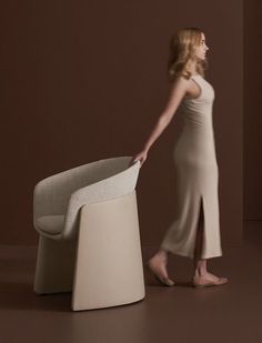 a woman standing next to a chair with her hand on the back of it's seat