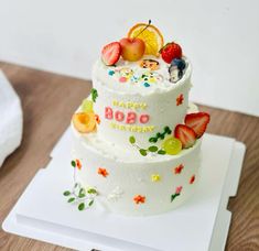 a three tiered cake with fruit on top and happy birthday written on the side