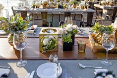 the table is set with silverware, plates and vases filled with white flowers