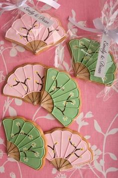 three decorated cookies in the shape of fan on a pink and white tablecloth with ribbon