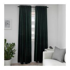 a living room with green curtains and a white couch in front of a window that has potted plants on it