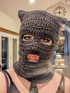 a woman wearing a crocheted hat and tie with a fake cat's head on her face