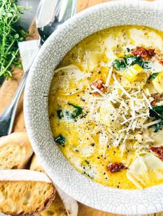 a white bowl filled with pasta and spinach soup next to slices of bread on a cutting board