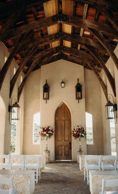 the inside of a church with white chairs and floral arrangements on the alter, doors are open