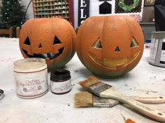 two pumpkins sitting on top of a table with paint and brushes next to them