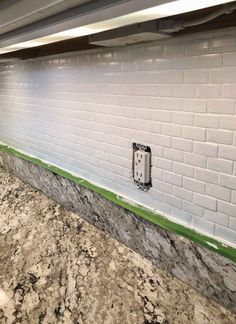 a white brick wall with green trim around the edges and an electrical outlet on it