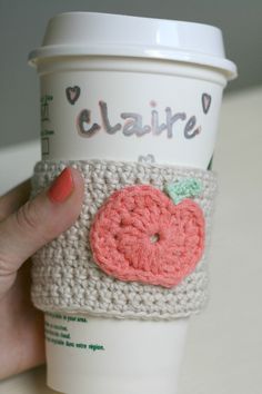 a woman's hand holding up a crocheted coffee cup sleeve with an apple on it