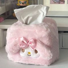 a pink stuffed animal with a tissue box on top of it's head and a doll in the background