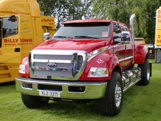 a large red truck parked on top of a lush green field next to other trucks