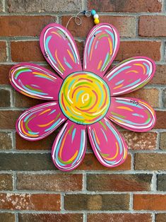 a flower painted on the side of a brick wall with a beaded necklace hanging from it