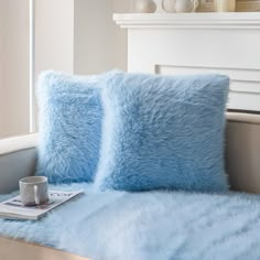 two blue pillows sitting on top of a bed next to a window sill with a cup