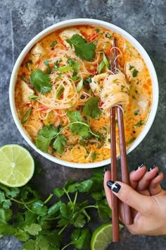 a person holding chopsticks in front of a bowl of noodles and cilantro