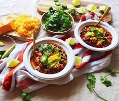 three bowls of chili with cheese, avocado and cilantro on the side