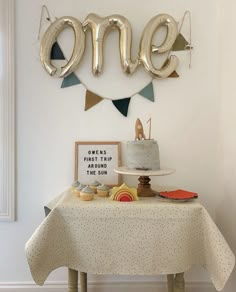 a table with a cake and balloons on it in front of a sign that says one