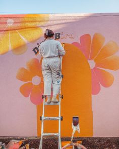 a person on a ladder painting a flowered wall with orange and pink flowers in the background