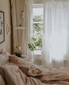 an unmade bed in front of a window with white curtains and flowers on it