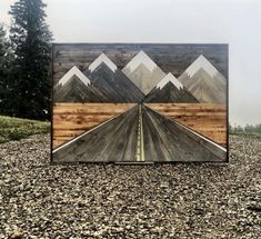 a wooden box sitting on top of a gravel covered field with mountains in the background