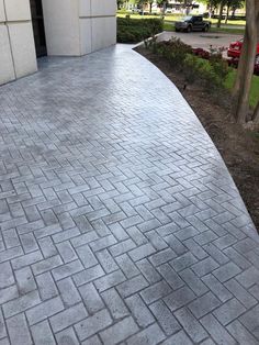 a brick walkway next to a building with cars parked on the side and trees in the background