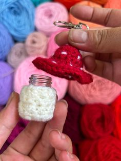 a person holding a tiny jar with a heart on it in front of some yarn