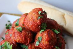 meatballs covered in marinara sauce and parsley on a plate next to a hot dog bun