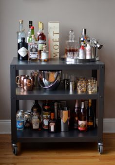 a bar cart filled with liquor bottles and glasses on top of wooden floor next to wall