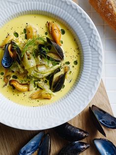 a white bowl filled with clams and some bread on top of a wooden table