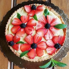 a pie topped with fresh strawberries and blackberries on top of a wooden table