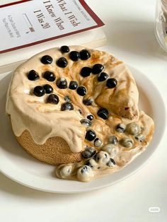 a white plate topped with a cake covered in frosting and black olives next to a book