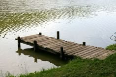 a wooden dock sitting in the middle of a lake surrounded by green grass and water