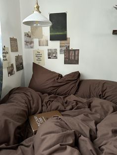 an unmade bed with brown sheets and pictures on the wall above it, along with a lamp