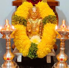 a golden buddha statue surrounded by yellow flowers and candles in front of a wooden bench