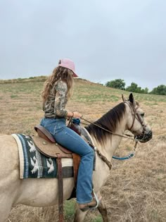 a woman riding on the back of a brown and white horse in a dry grass field