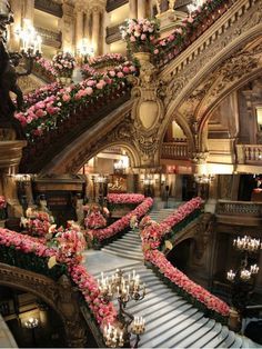 an ornate staircase decorated with pink flowers and chandeliers in a fancy hotel lobby