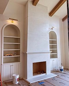 a fireplace being built in the middle of a room with white walls and wood beams