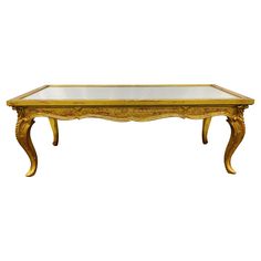 an antique coffee table with glass top and gold trimmings on the legs, against a white background