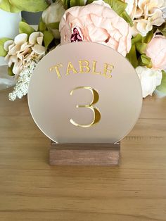 a table number is placed on top of a wooden stand with flowers in the background