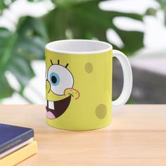 a yellow mug with a cartoon character on it sitting on a table next to a book