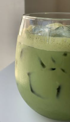 a glass filled with green liquid sitting on top of a white table next to a wall