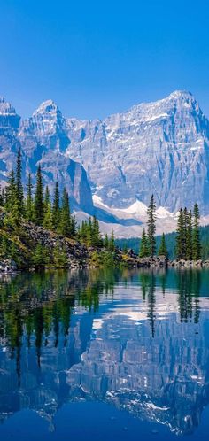 the mountains are reflected in the still water on the lake's surface, while pine trees stand at the edge