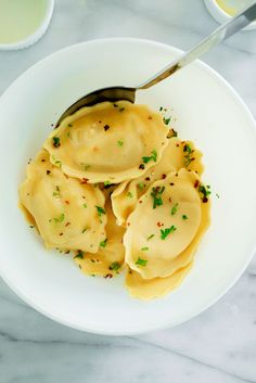 a white bowl filled with dumplings and sauce on top of a marble countertop