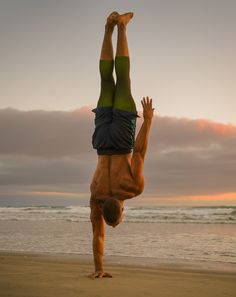 a man doing a handstand on the beach at sunset with his feet in the air