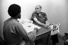 two men sitting at a table with papers in front of them and one man reading the paper