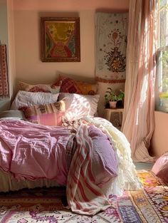 a bed with pink sheets and pillows in a bedroom next to a window filled with curtains