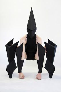 a person sitting on the ground with their legs spread out in front of them, wearing an origami mask