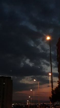 the sky is dark and cloudy at night with street lights lit up in the distance