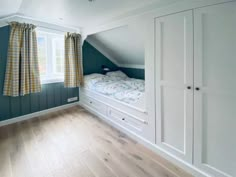 an attic bedroom with green walls and wooden floors, built - in closets, and white bedding