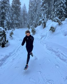 a woman riding skis down a snow covered slope next to evergreen trees in the background